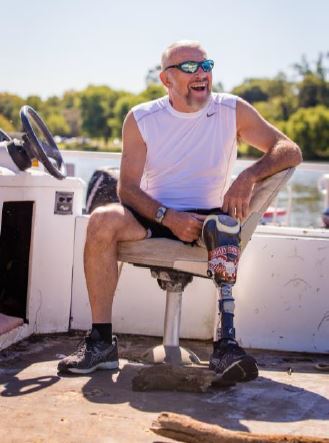 Man with a prosthetic leg sitting in a chair on a small boat in a lake.