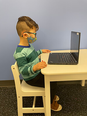 Young boy sitting at a small desk and using a laptop.