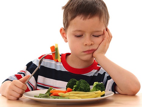 Young boy holding fork and staring unhappily into a plate of vegetables.
