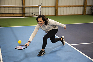 Woman diving for small ball on pickleball court.