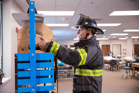 Male fireman in full fire gear practicing safe lifting in a therapy gym.