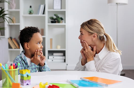 Child and speech-language pathologist sit together at a table to complete speech exercises