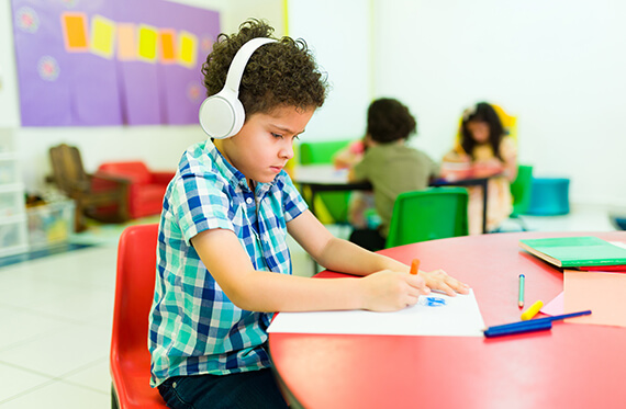 Child at school wearing headphones and coloring at a desk